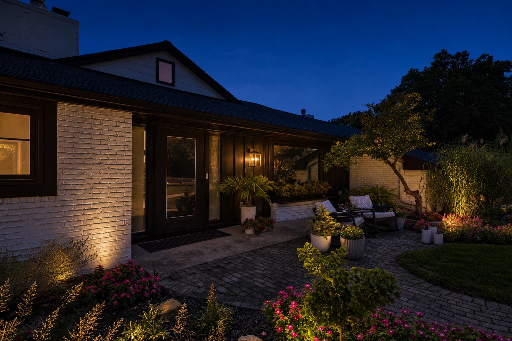 Close view of the illuminated front entry, brick walk, seating area, and landscaping