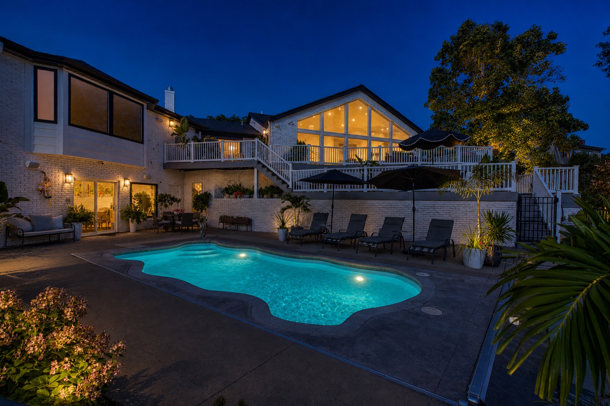 Illuminated backyard pool and rear terrace beneath the home’s wall of windows at twilight