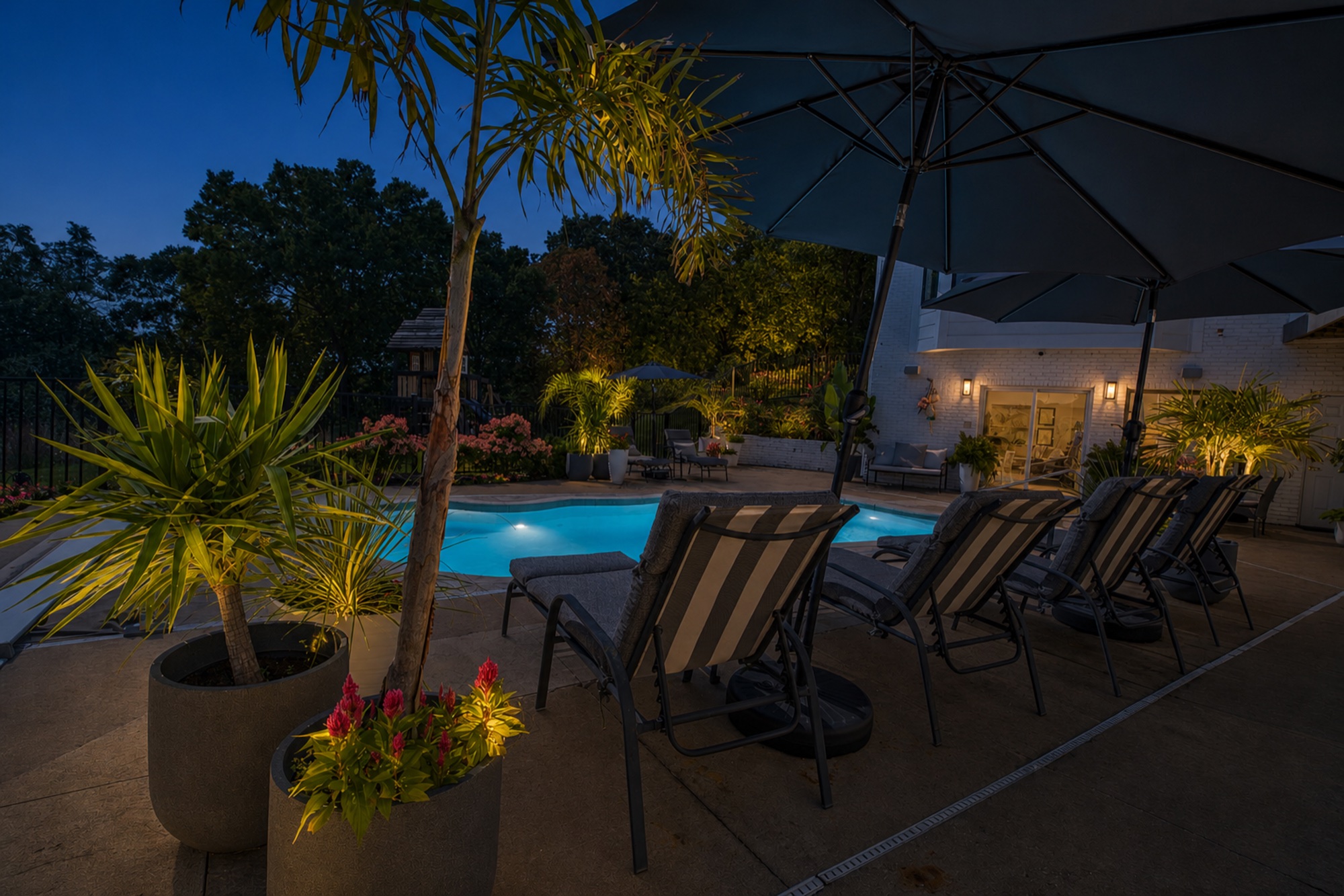 Pool terrace with lounge seating, umbrellas, tropical planters, and subtle landscape lighting